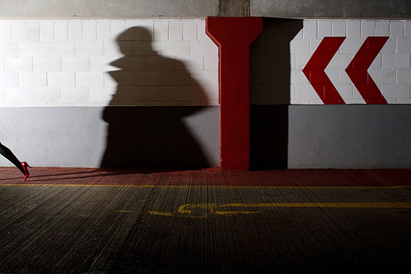 Woman's high-heeled foot exiting the far left of frame and casting a threatening shadow on the wall behind her in a multi storey car park