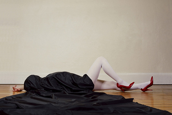 Woman wearing red high-heeled shoes lying on the floor covered in black silk